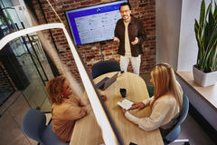 2 females sitting at a table and male standing in front of a screen explaining