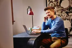 Male in a blue shirt sitting at a desk working on his laptop