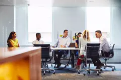 Group of colleagues sitting down in a meeting room at the office, smiling.
