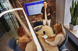2 females sitting at a table and male standing in front of a screen explaining