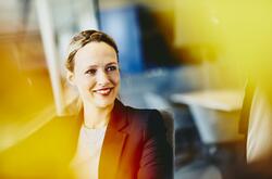 Woman in suit in an office smiling. Primary color: yellow.
