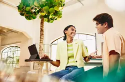 male and female sitting at table having a chat, while female working on a tablet.
