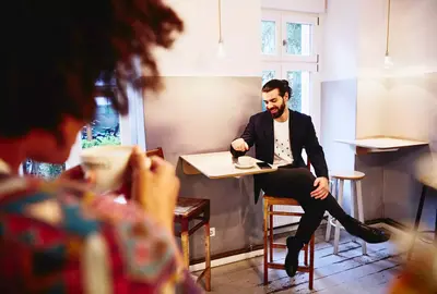 male sitting at a table with coffee, looking down while having a conversation with someone.
