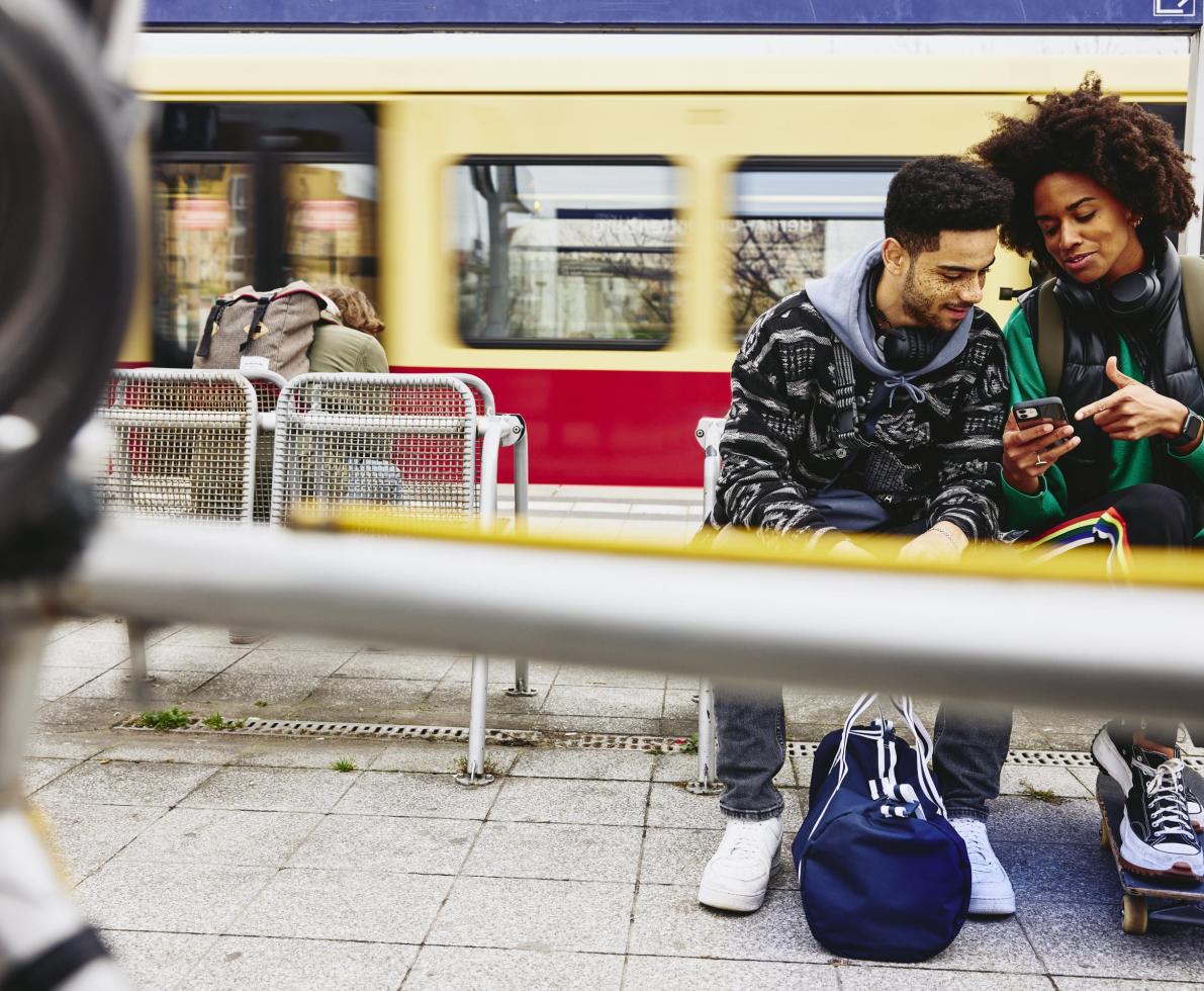 Man and woman looking at phone while sitting on a bench on a train platform.