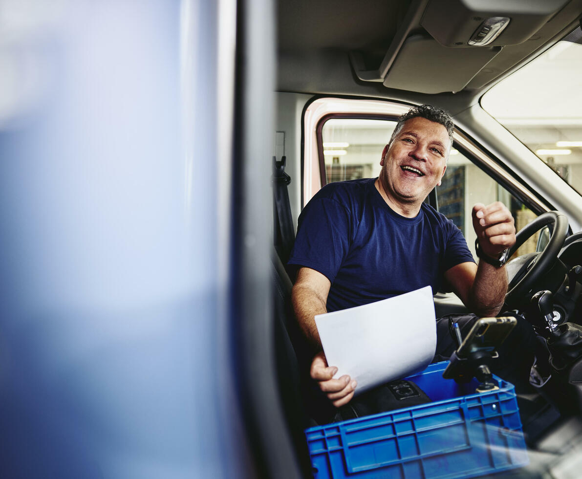 Smiling male sitting in driver's seat of a logistics truck holding a piece of paper
Smiling male sitting in driver's seat of a logistics truck holding a piece of paper