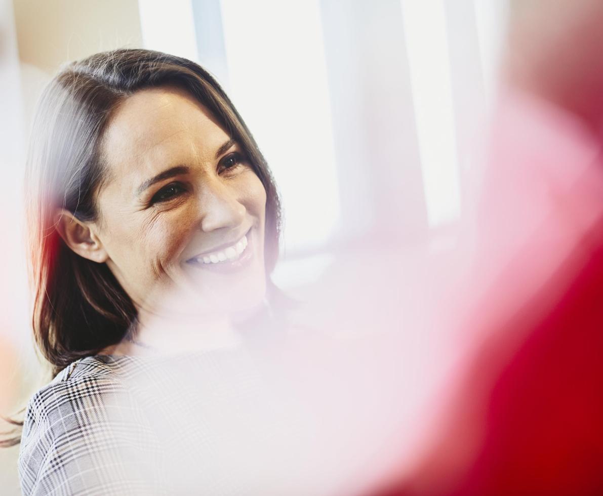 Woman in an office smiling. Primary color: red.