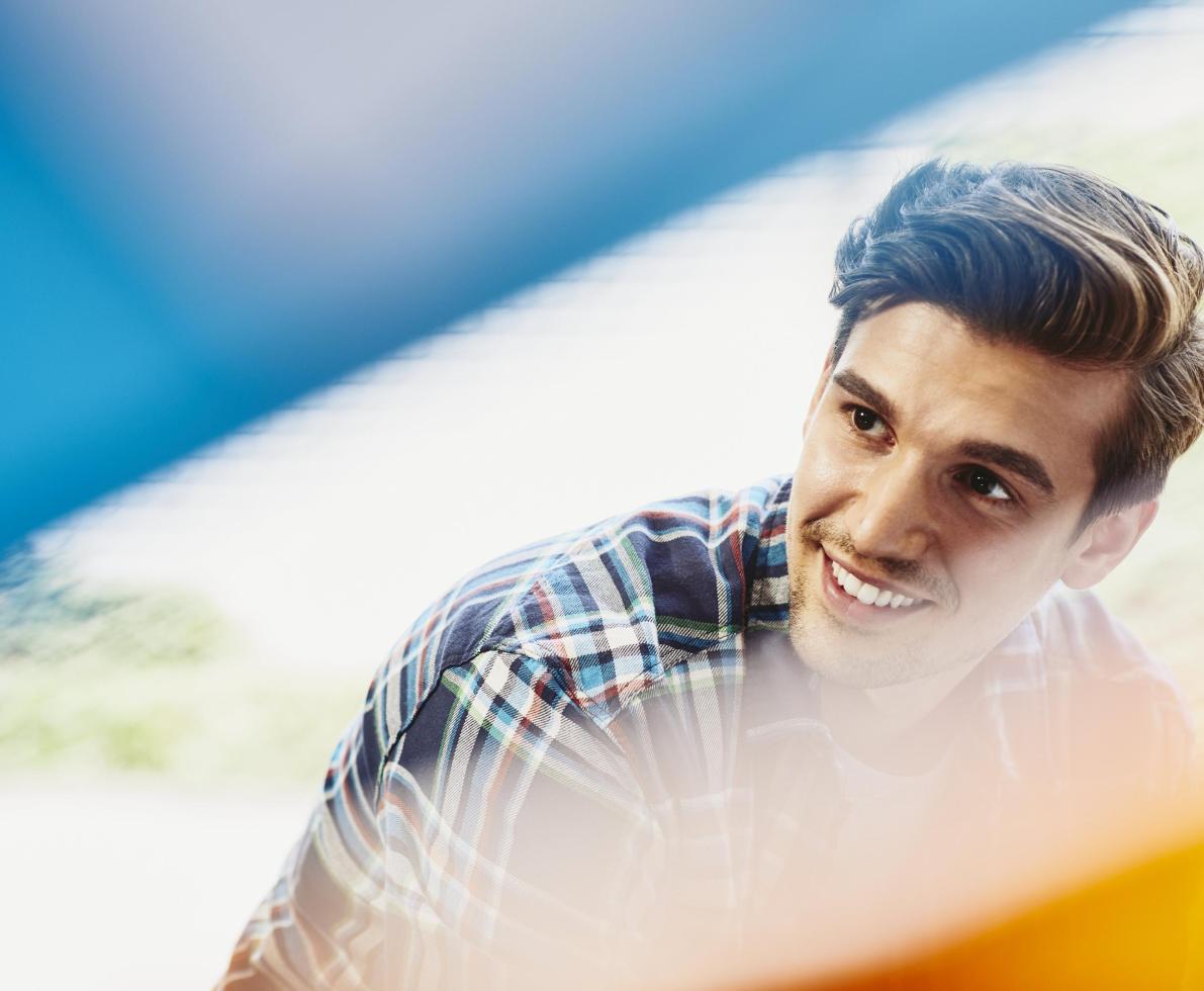 Male employee smiling and looking to his right. Groomed beard and mustache. Wearing a checkered shirt. Primary color blue. Secondary colors cream and yellow. ένας άνδρας χαμογελάει