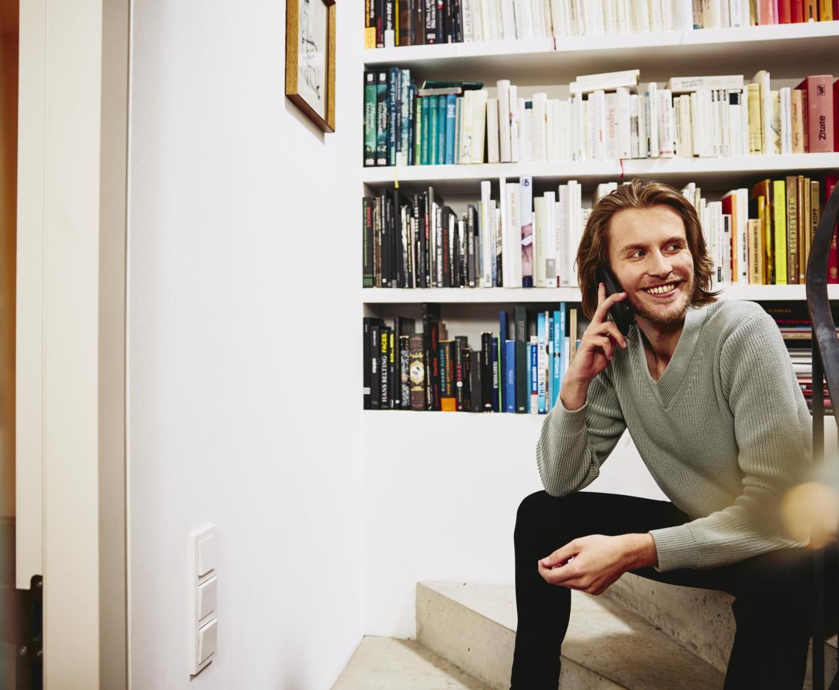 Smiling man sitting on stairs, having a phonecall. bookshelf in background χαμογελαστός άνδρας κάθεται στις σκάλες