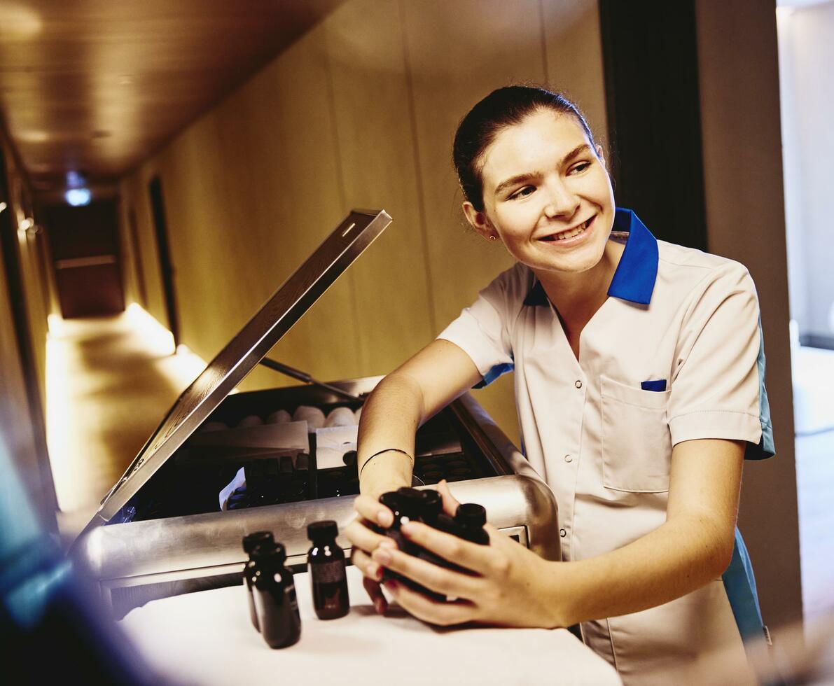 Woman in housekeeping uniform, holding small toiletries bottles.