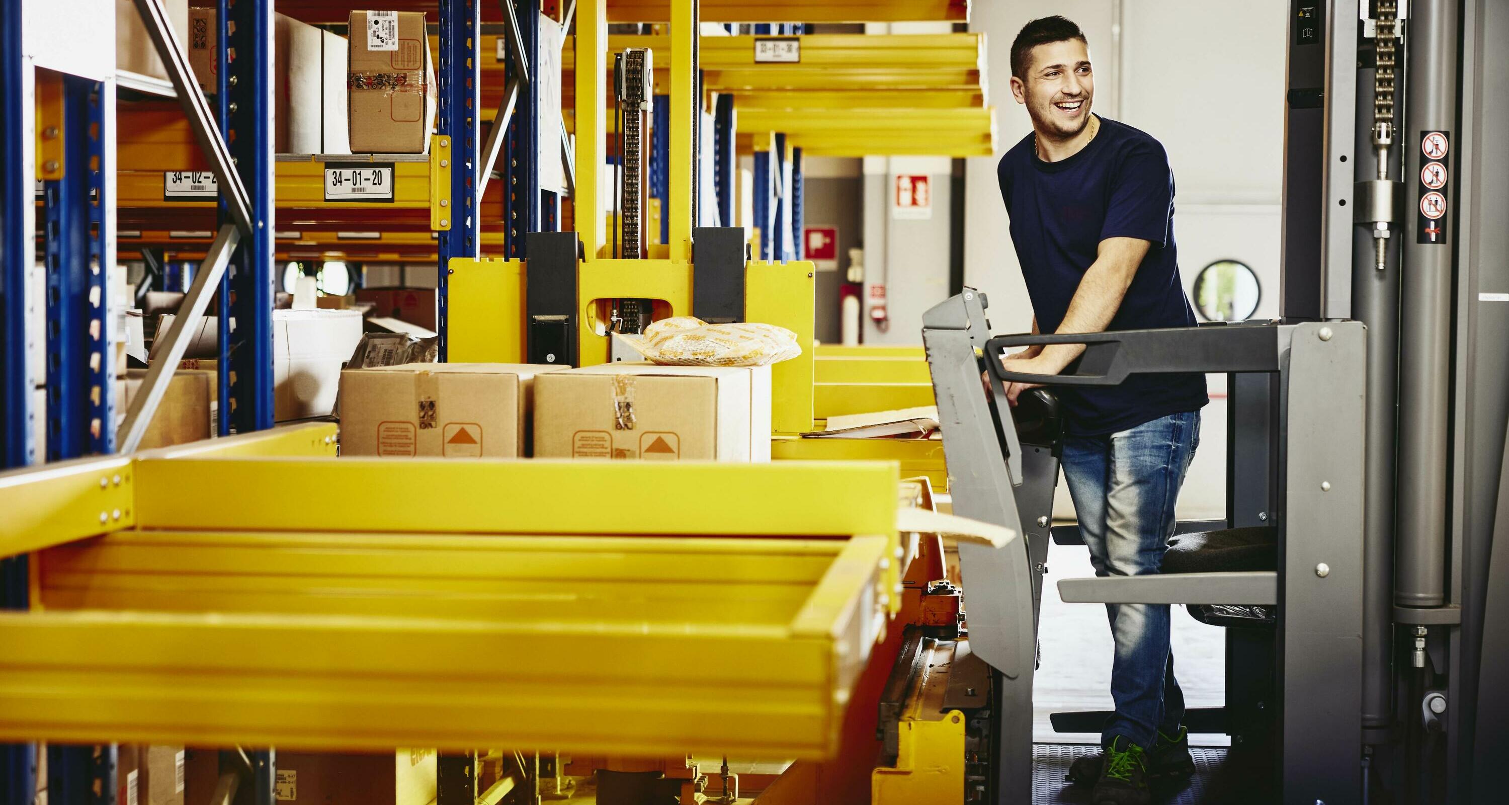 Smiling male standing on a forklift.